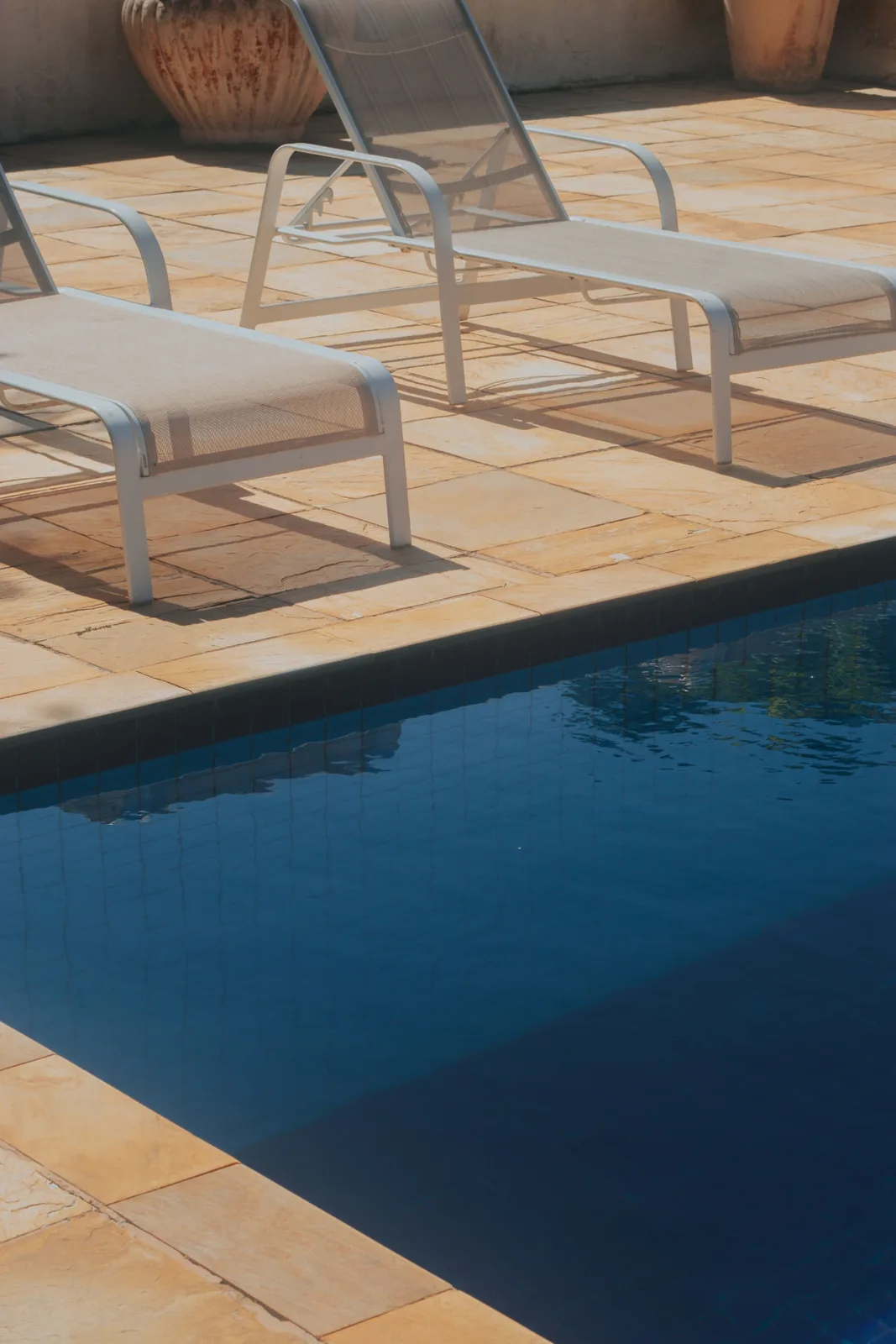 Borda de piscina com piso externo em placas de pedra e espreguiçadeiras ao sol